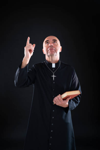 istock Priest bald pointing finger to heaven up holding bible 1193047478