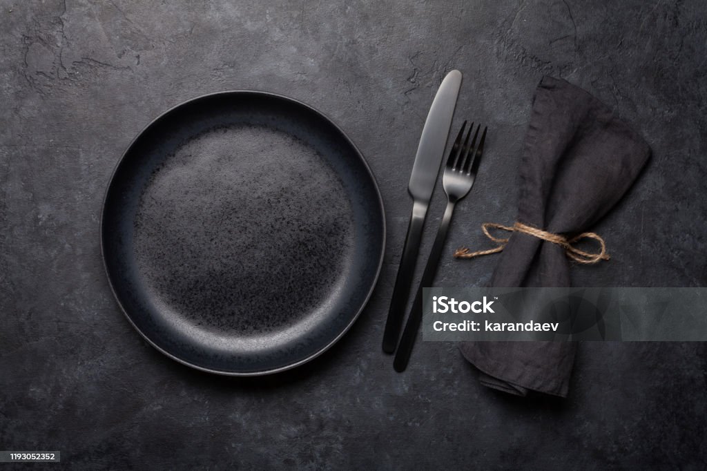 Empty plate, fork and knife Empty plate, fork and knife. Black kitchen utensils set on stone table. Top view flat lay with copy space Plate Stock Photo