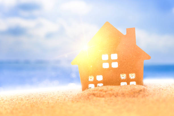 istock Closed up tiny home models on sand with sunlight and beach background.Investment property concept. 1193054787