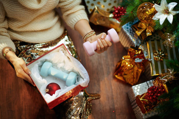 ama de casa sosteniendo la caja de regalo de navidad y mancuernas - holiday healthy lifestyle weight christmas fotografías e imágenes de stock