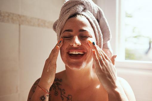 Shot of a young woman giving herself a facial at home