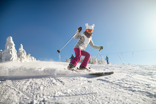 Teenage girl skiing on a beautiful sunny winter day.  The girl is speeding on a modern wide ski slope.\nNikon D850
