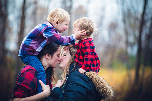 Children, Couple, Family - Lesbian couple kissing each other while carrying their kids on the shoulder