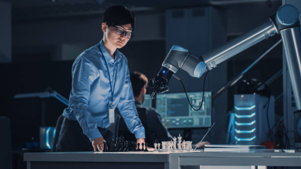 ingeniero profesional de desarrollo japonés está probando una interfaz de inteligencia artificial jugando ajedrez con un brazo robótico futurista. están en un laboratorio de investigación moderna de alta tecnología. - chess pawn red blue leisure games fotografías e imágenes de stock