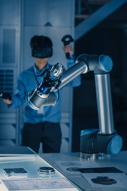 vertikale aufnahme von professionellen entwicklungsingenieur in blauen shirt steuerung futuristischen roboterarm mit virtual reality headset und joysticks in einem high-tech-forschungslabor mit moderner ausrüstung - arm anatomiebegriff grafiken stock-fotos und bilder