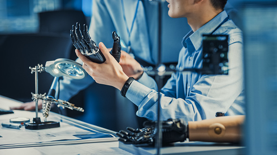 El brazo de robot protésico tecnológico es probado por dos ingenieros de desarrollo profesional en un laboratorio de investigación de alta tecnología con equipos futuristas modernos. Compare los datos en un ordenador personal. photo