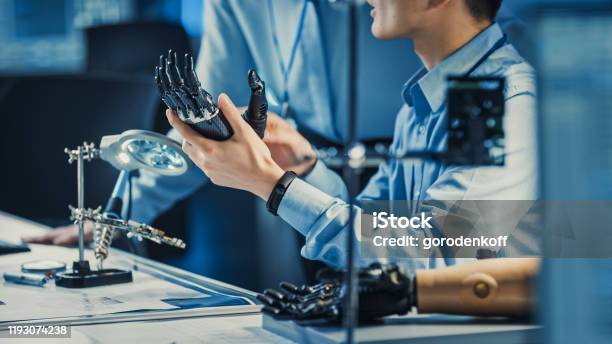 Technological Prosthetic Robot Arm Is Tested By Two Professional Development Engineers In A High Tech Research Laboratory With Modern Futuristic Equipment Compare Data On A Personal Computer Stock Photo - Download Image Now