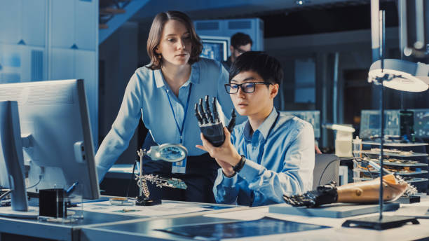 istock Technological Prosthetic Robot Arm is Closely Tested by Two Professional Specialists in a High Tech Research Laboratory with Modern Futuristic Equipment. Man and Female Talk and Ananlyse the Object. 1193074281