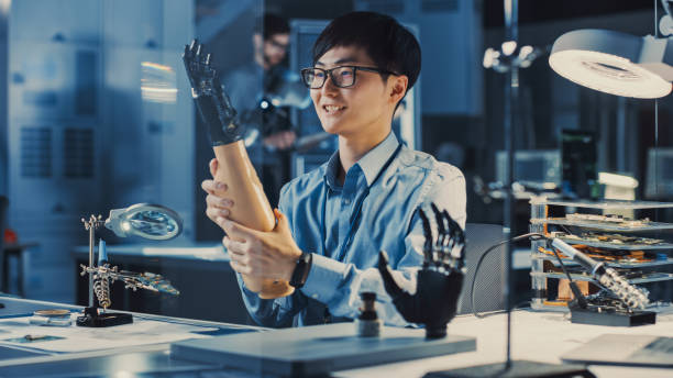 istock Futuristic Prosthetic Robot Arm Being Tested by a Professional Japanese Development Engineer in a High Tech Research Laboratory with Modern Computer Equipment. He is Satidfied with the Result. 1193074352