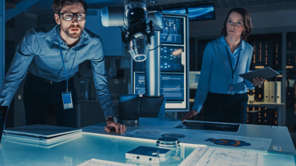 istock Futuristic Robotic Arm Moving and Placing a Metal Object. Senior Engineer Talks Through This Advanced Process. They are in a High Tech Research Laboratory with Modern Equipment. 1193074392
