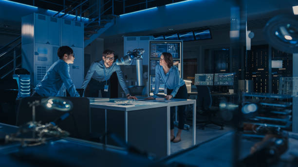 istock Futuristic Metal Robotic Arm is Moving a Metal Object. Senior Engineer Talks Through This Advanced Process with His Diverse Team. They are in a High Tech Research Laboratory with Modern Equipment. 1193074953