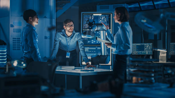 istock Diverse Team of Engineers with Laptop and a Tablet Analyse and Discuss How a Futuristic Robotic Arm Works and Moves a Metal Object. They are in a High Tech Research Laboratory with Modern Equipment. 1193075006