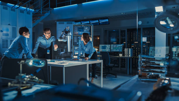 istock Futuristic Metal Robotic Arm is Moving a Metal Object. Senior Engineer Talks Through This Advanced Process with His Diverse Team. They are in a High Tech Research Laboratory with Modern Equipment. 1193075014