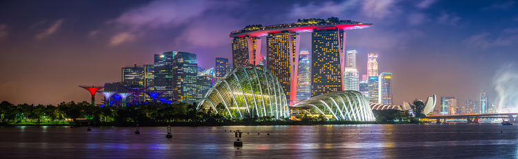 Panoramic vista across the iconic landmarks of Singapore, from the glittering skyscrapers of the Downtown Core, past the futuristic towers of Marina Bay Sands to the Gardens by the Bay all illuminated at night.
