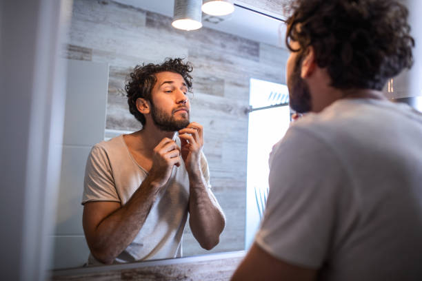 istock Reflection of handsome man with beard looking at mirror and touching face in bathroom grooming 1193083280