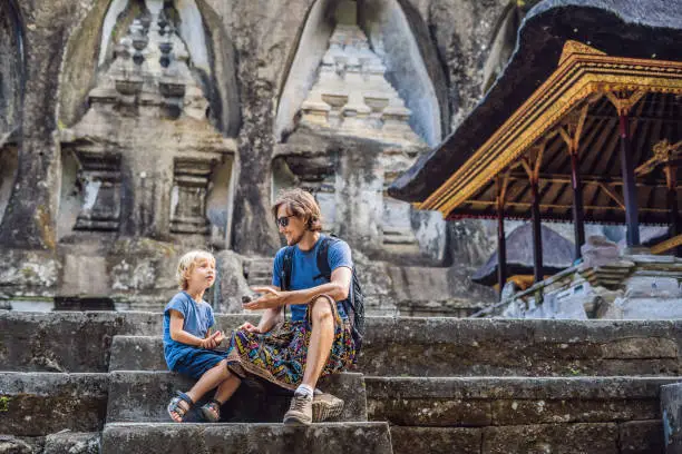 Photo of Dad and son on background of Gunung Kawi. Ancient carved in the stone temple with royal tombs. Bali, Indonesia. Traveling with children concept