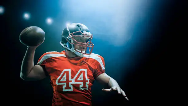 American football player throwing ball against black background.
