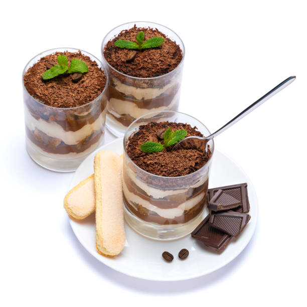 Classic tiramisu dessert in a glass cup on the plate and pieces of chocolate on white background with clipping path