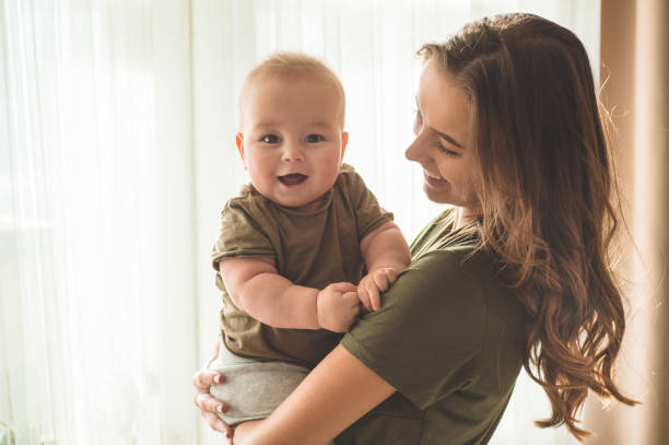 Home portrait of a baby boy with mother near the window. Mom holding and kissing her child. Home portrait of a baby boy with mother near the window. Mom holding and kissing her child. Mother day concept cute boy show love symbol hand stock pictures, royalty-free photos & images