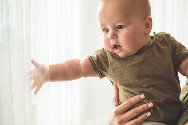 Home portrait of a baby boy with mother near the window. Mom holding and kissing her child. Home portrait of a baby boy with mother near the window. Mom holding and kissing her child. Mother day concept cute boy show love symbol hand stock pictures, royalty-free photos & images