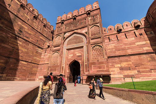 Agra, Uttar Pradesh, India - March 2019: Tourists walk around the historic Delhi gate inside the ancient Agra Fort built by the Mughal Emperor Akbar.