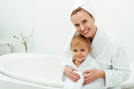 happy mother smiling while hugging toddler boy in bathroom