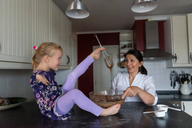 Little girl with no arms make cake with her mother Limitless little girl with no arms uses a wire whisk to mix cake batter. She is holding the whisk with her feet. Her mom smiles as she holds up the whisk. chocolate fingers stock pictures, royalty-free photos & images