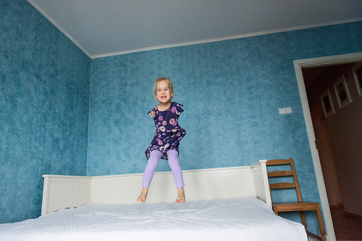 Little girl with no arms smiles while jumping on the bed in her room.