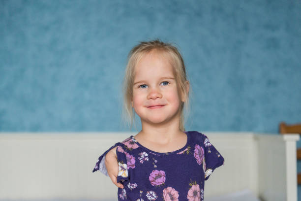 Adorable little girl with no arms and limited use of one hand smiles cheerfully at the camera while at home.