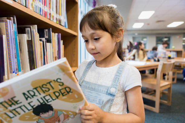 istock Cute elementary age girl enjoys storybook at library 1193114179