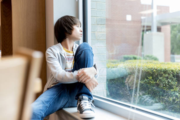 istock Lonely middle school boy sits on windowsill at school 1193114221