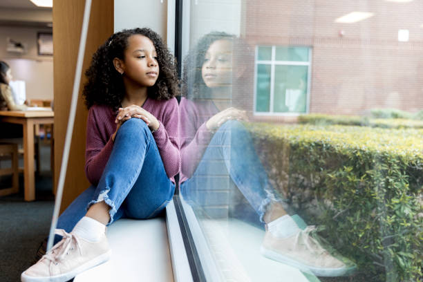 Young girl daydreams while looking out library window The young girl sits on the windowsill at the library as she looks out the window and daydreams. junior high photos stock pictures, royalty-free photos & images