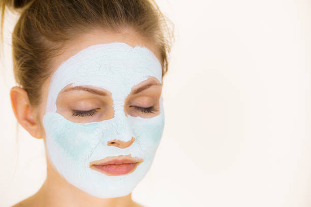 Young woman with green mud mask on face, on white. Teen girl taking care of oily skin, purifying the pores. Beauty treatment. Skincare.
