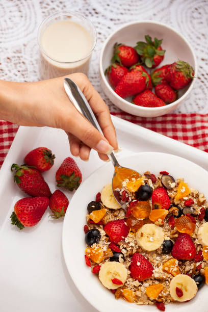 primo piano della mano prendendo l'avena da un piatto attraverso il cucchiaio. - nut snack fruit healthy eating foto e immagini stock