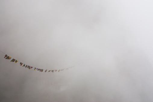 Prayer flags barely visible through thick fog clouds at the famous Tiger's Nest temple, Paro, Bhutan