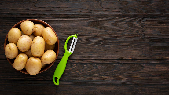 Young unpeeled potatoes in a bowl on a wooden dark table.