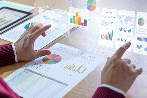 Businessman interacts with augmented reality graphics while deeply reviewing a financial report for a return on investment or investment risk analysis.