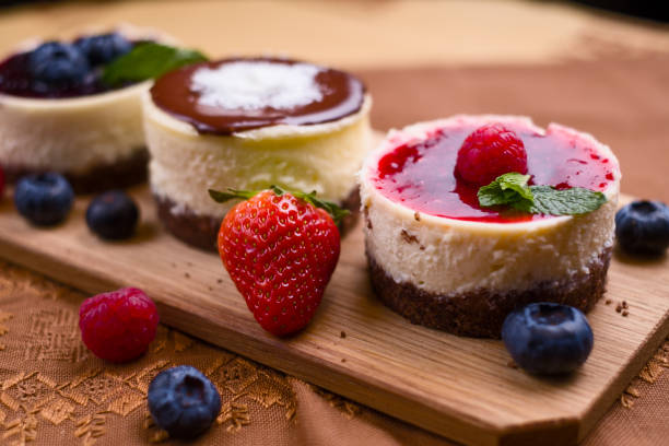 Three mini oval cheesecakes, one with raspberry sauce and berries Three mini oval cheesecakes, one with raspberry sauce and berries decoration on brown cloth and wooden pad wedding cake close up macro stock pictures, royalty-free photos & images