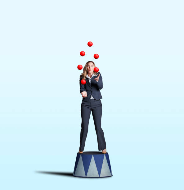 Businesswoman Juggling Red Balls A businesswoman stands on a circus pedestal as she juggles a group of red balls isolated on a light blue background. juggling stock pictures, royalty-free photos & images
