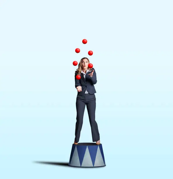 A businesswoman stands on a circus pedestal as she juggles a group of red balls isolated on a light blue background.