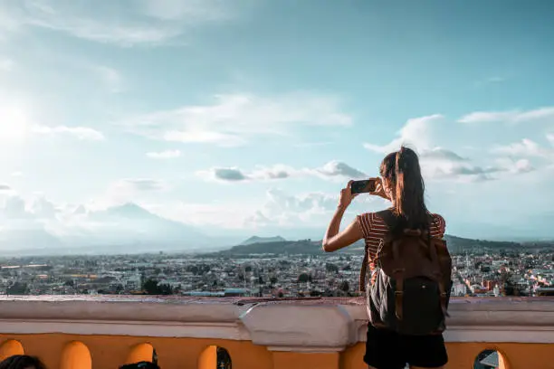 Young woman standing at the balcony and taking pictures of the city