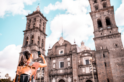 Young woman taking a photo of Cathedral Basilica de Puebla with her smartphone