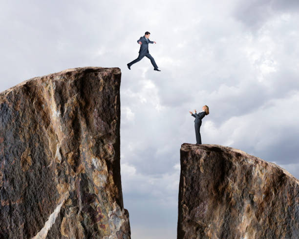 Businessman Jumps From One Cliff To Another A businessman takes a leap of faith as his female colleague looks up at him from below. leap of faith stock pictures, royalty-free photos & images