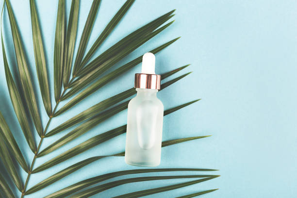 Serum bottle on palm leaf. Blue background. Serum bottle on palm leaf. Trendy beauty product for young skin. Additional moisturizing step in everyday facial routine. Flat lay, top viev. glass medicine blue bottle stock pictures, royalty-free photos & images