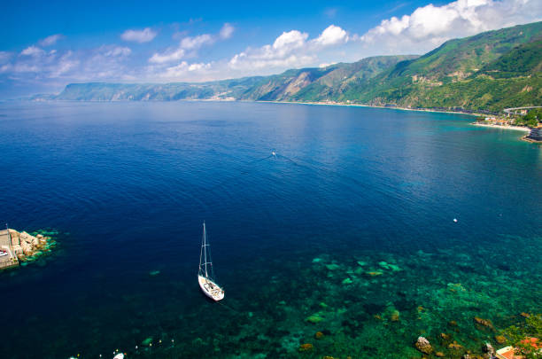 White yacht in blue lagoon near small fishing village, Calabria, Italy Aerial top view of white yacht ship boat in blue lagoon near small fishing village Chianalea di Scilla from castle on rock Ruffo, Mediterranean Tyrrhenian sea coast shore, Calabria, Southern Italy castle scilla stock pictures, royalty-free photos & images
