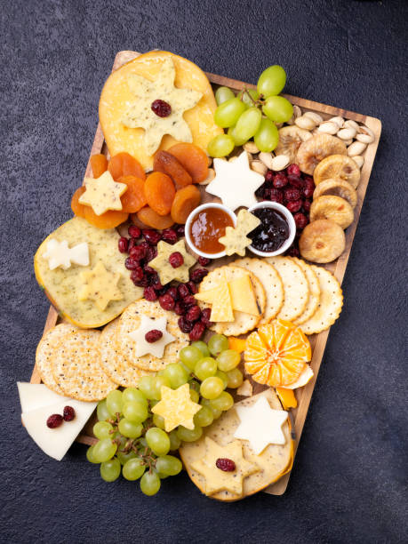 istock Assorted cheeses on wooden board plate hard cheese slices, walnuts, grapes, crackers, chutney mango, jam, dark background, top view. Copy space. 1193150947
