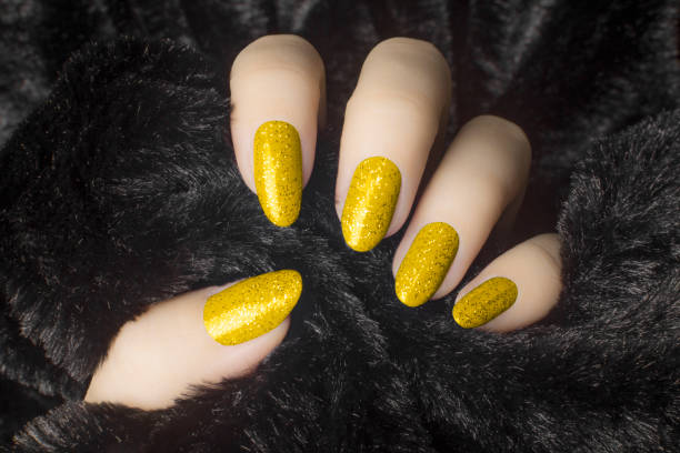 glittered yellow nails manicure Female hand with glittered yellow nails is holding black fur, manicure and nail care concept. yellow nail polish stock pictures, royalty-free photos & images