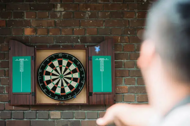 Photo of Asian man aiming and throwing dart at dartboard of his house
