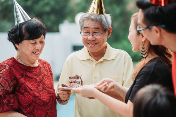 アジアの中国のシニア男性は、スイミングプールの横にある家の前庭で誕生日パーティーを祝っている間に彼の素敵な家族からケーキを受け取りました - swimming swimming pool senior adult child ストックフォトと画像