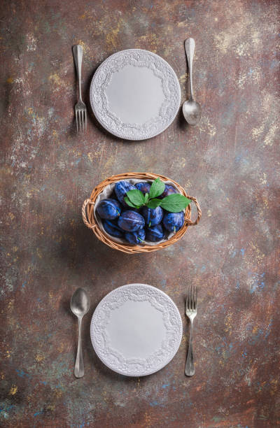Plums with white plates forks and spoons table overhead arrangement
